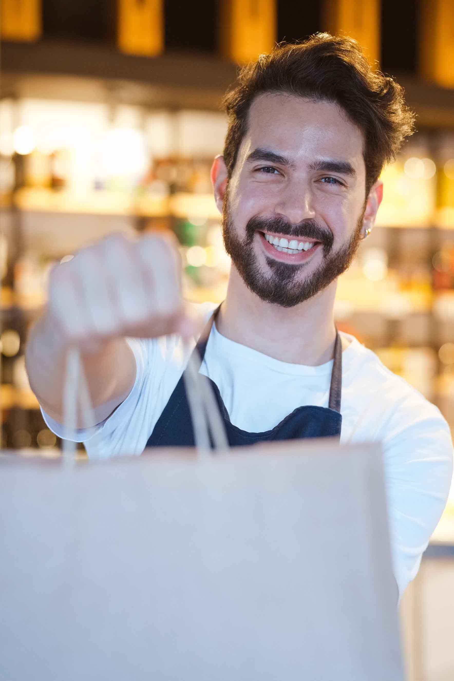 Smiling Caspian Market staff holding a shopping bag, ready to serve customers